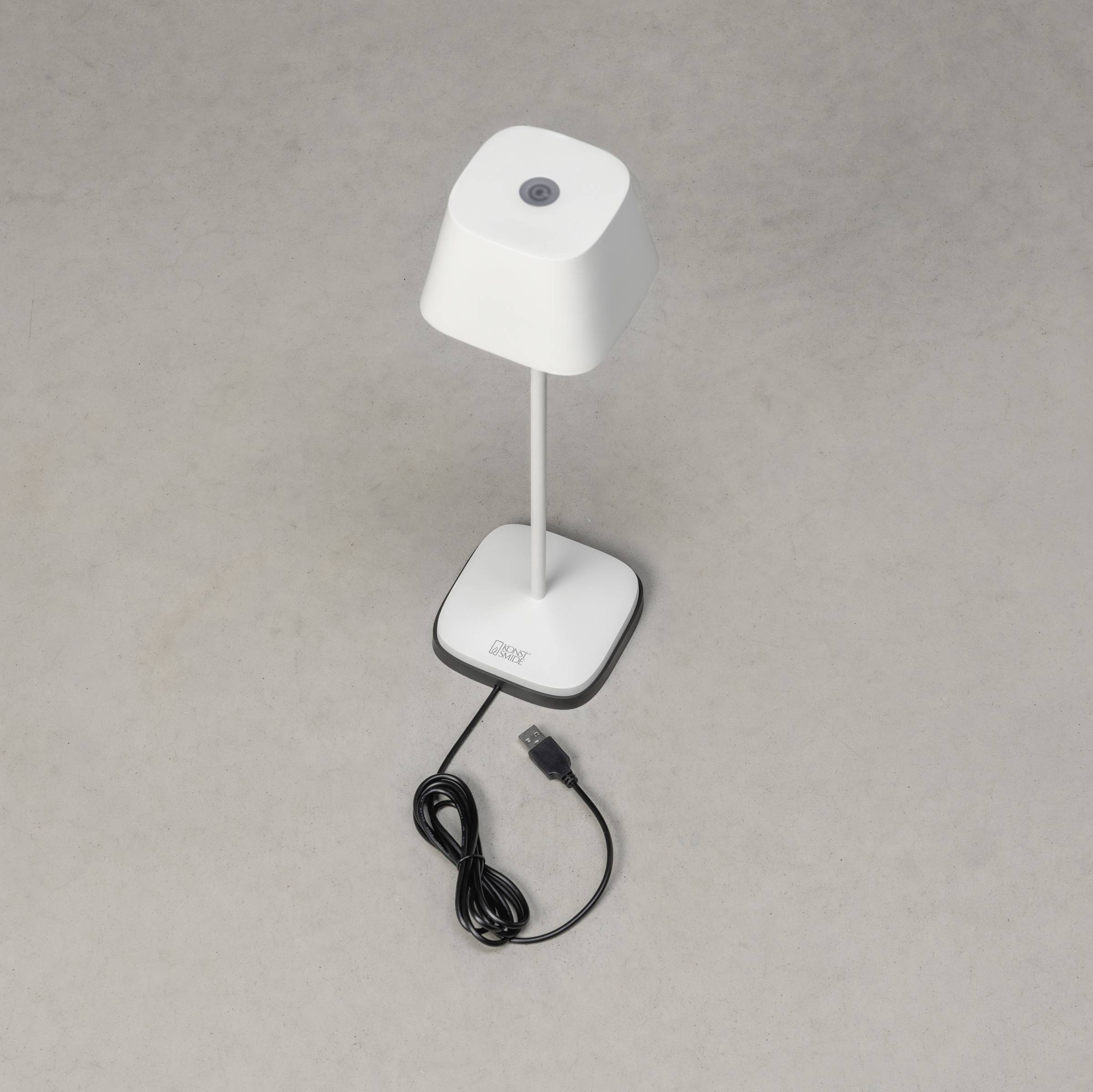 Hvid bordlampe med firkantet skærm og USB-kabel på grå baggrund.