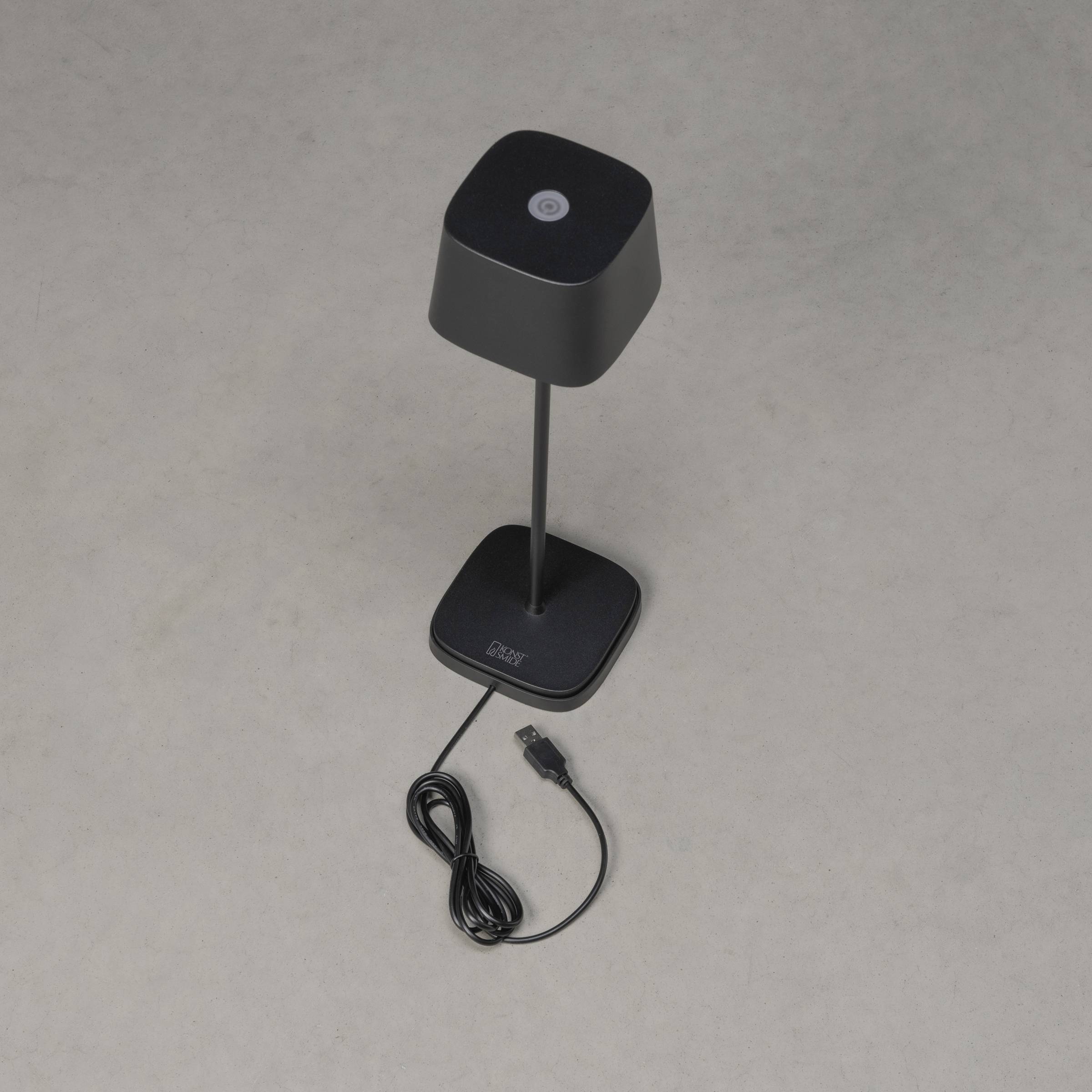 En sort bordlampe med USB-stik ligger på et gråt underlag. Lampeskærmen er firkantet, og kablet er løst viklet op.