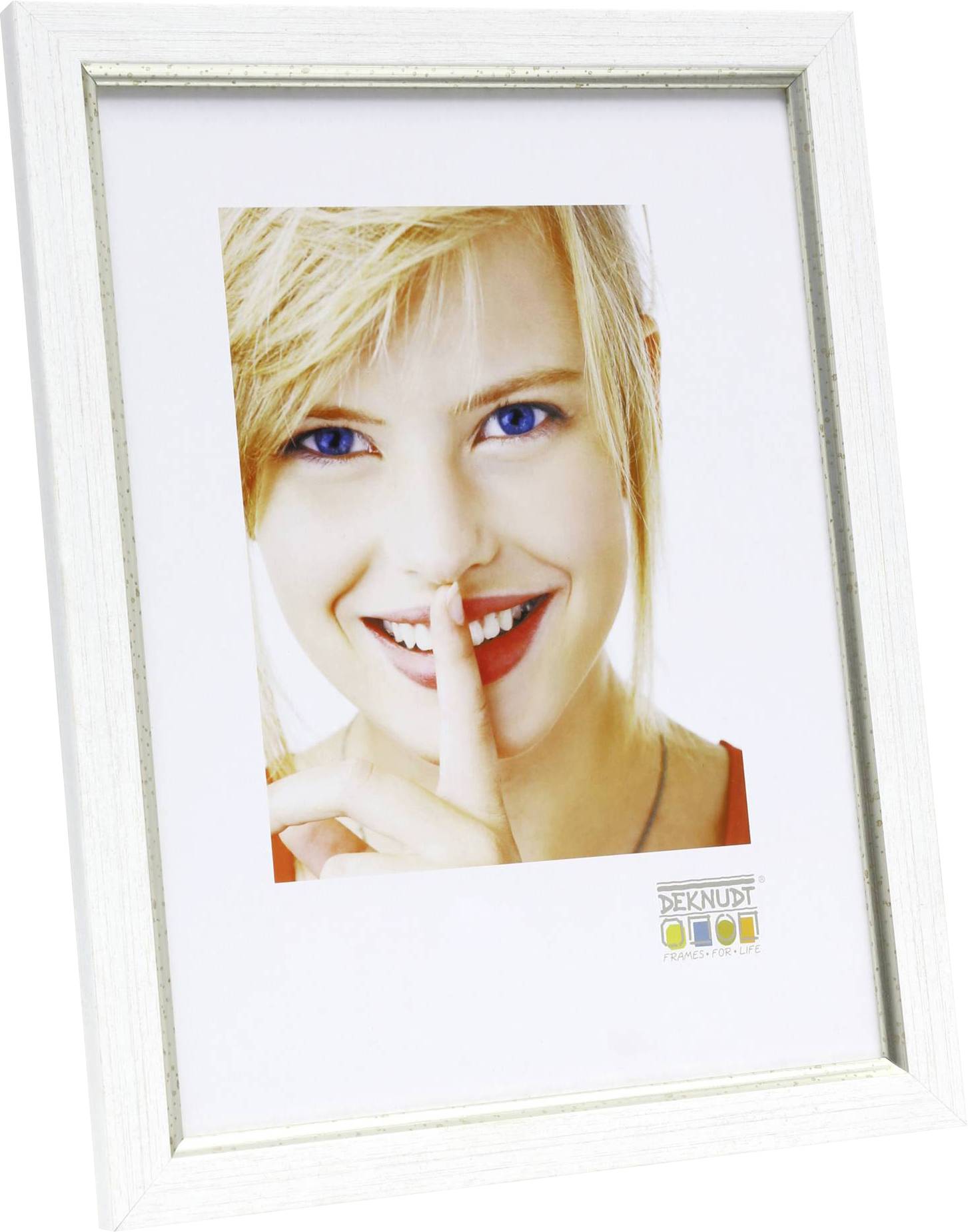 En smilende person med blondt hår holder en finger foran læberne som tegn på tavshed. Vedkommende kigger direkte ind i kameraet.