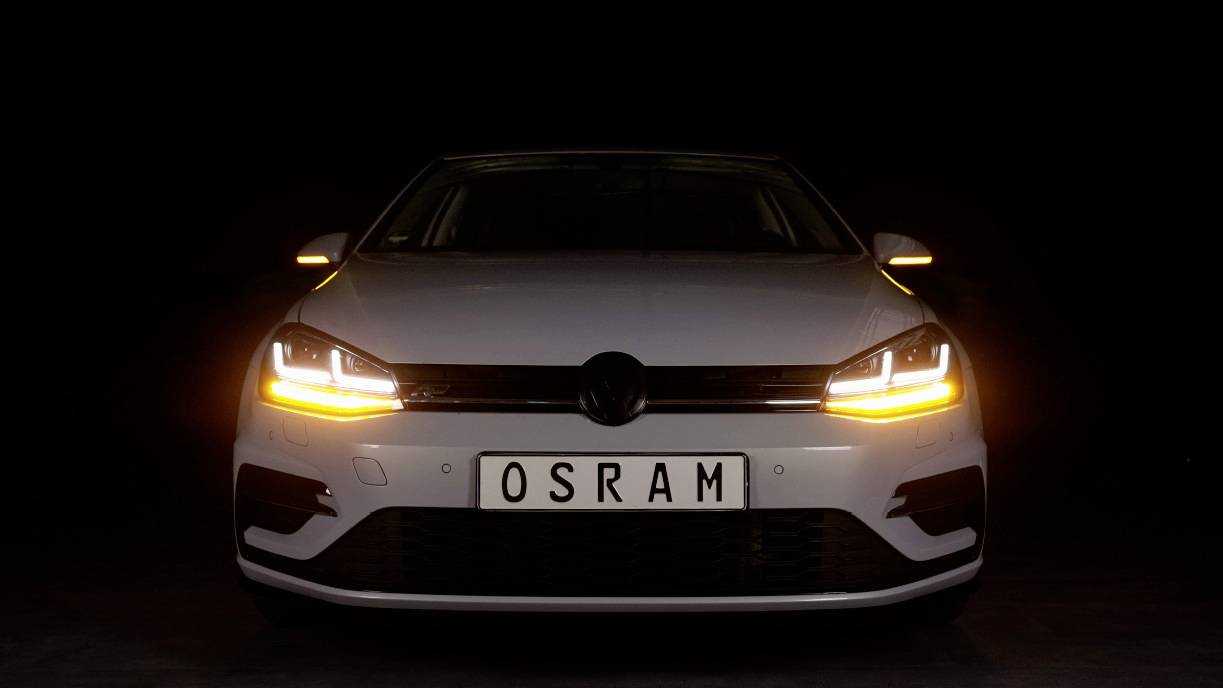 Bil i mørket, forlygter lyser gul-orange, nummerplade 'OSRAM'.