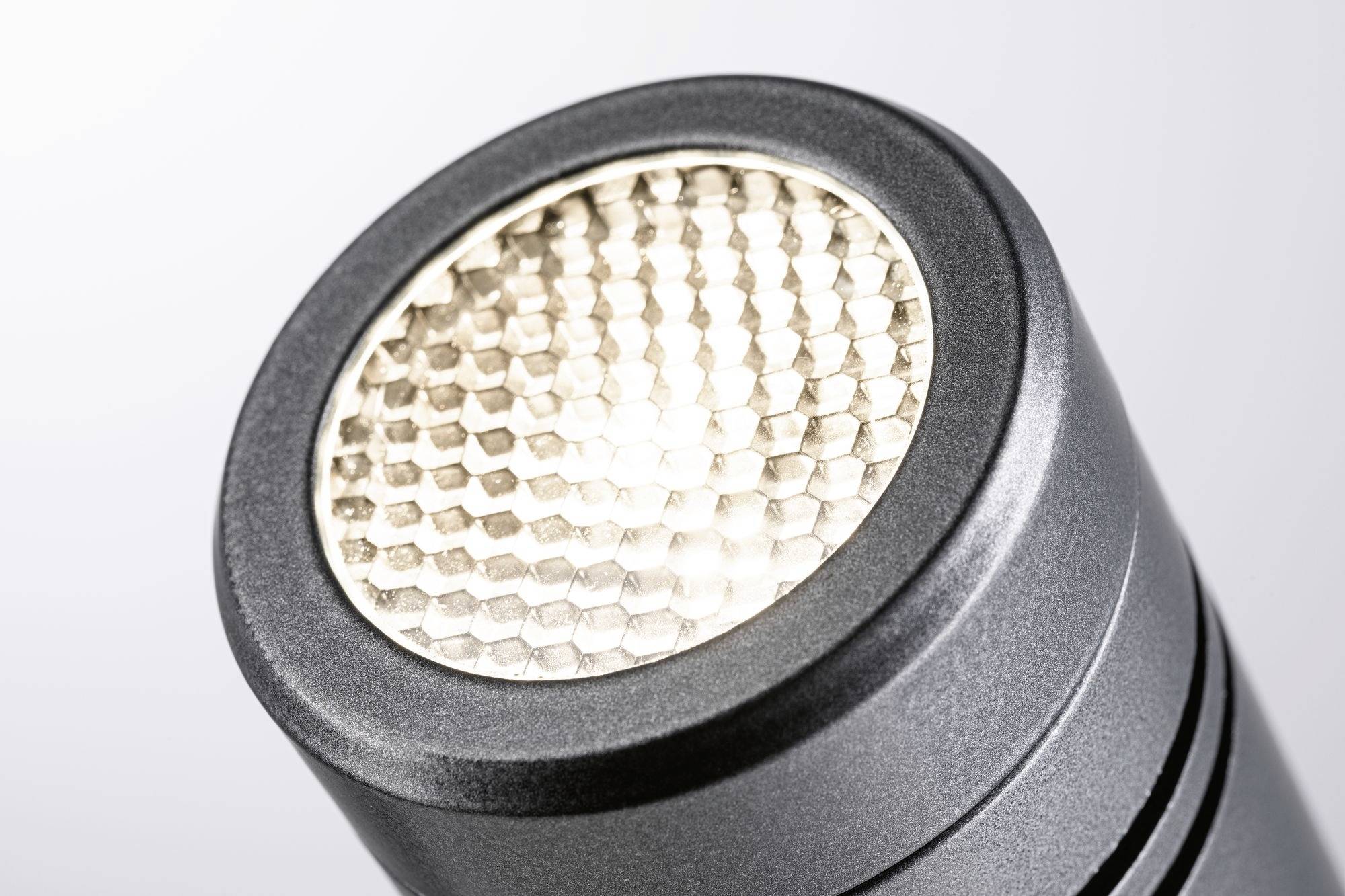 Nærbillede af en lysende LED-lommelygte med honeycomb-formet linse foran en lysegrå baggrund.