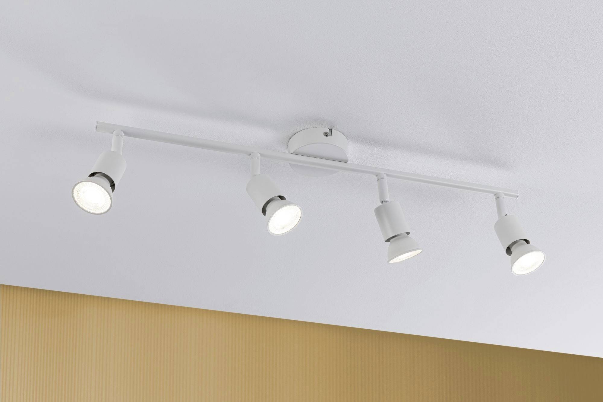 En hvid loftslampe med fire justerbare spots, monteret på en glat lofteflade, oplyser rummet ensartet.