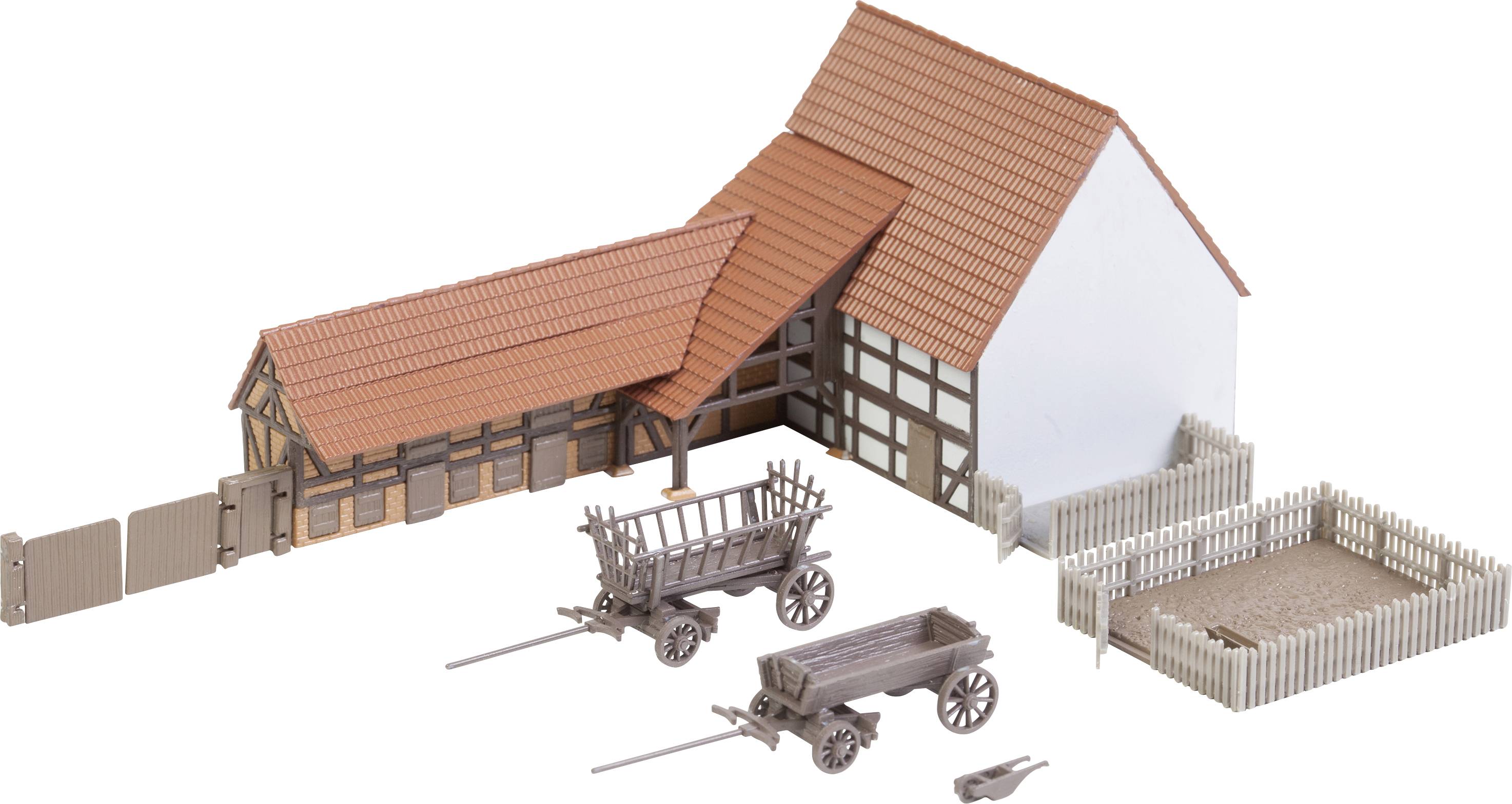 Miniaturemodel af et bindingsværksgårdhus med rødt tag, to trækvogne og hegn, placeret på en hvid baggrund.