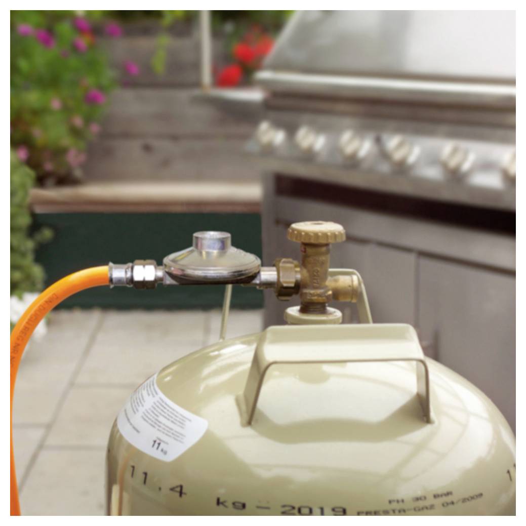 Nærbillede af en propantank forbundet til en grill via en orange slange og regulator udendørs.