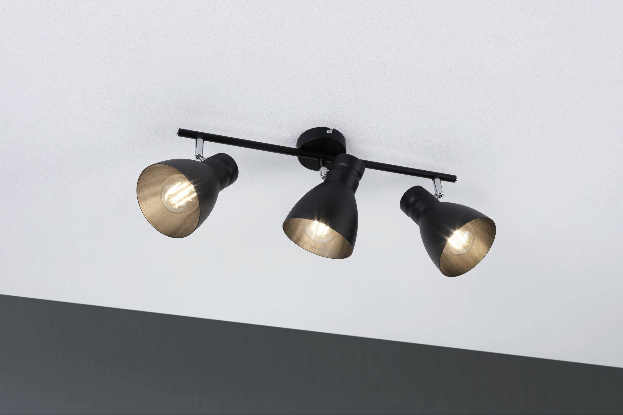 En treflasket sort loftslampe med justerbare spots monteret i loftet, som lyser i forskellige retninger.