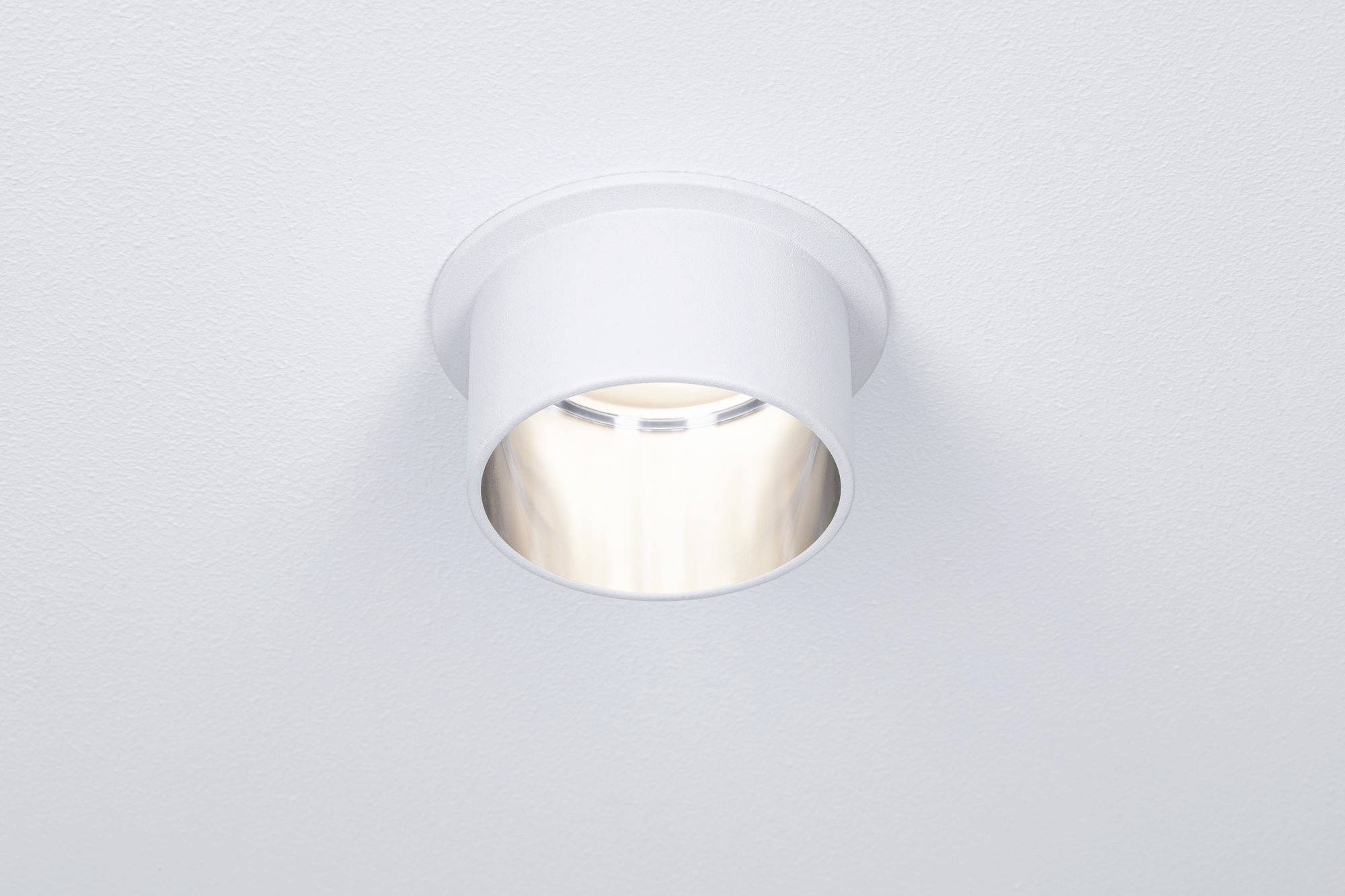 Loftslampe med rund, hvid kabinet, plan monteret i loftet, som afgiver varmt, indirekte lys.