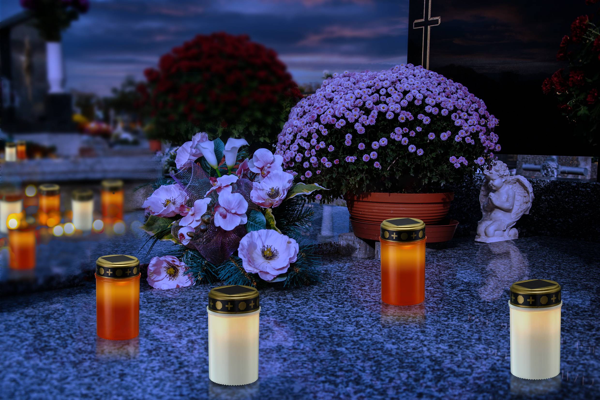 Grave ved tusmørke med gravlys og blomsterpryd; i baggrunden lyser lys, og en engel-statue står ved siden af blomsterpotter.