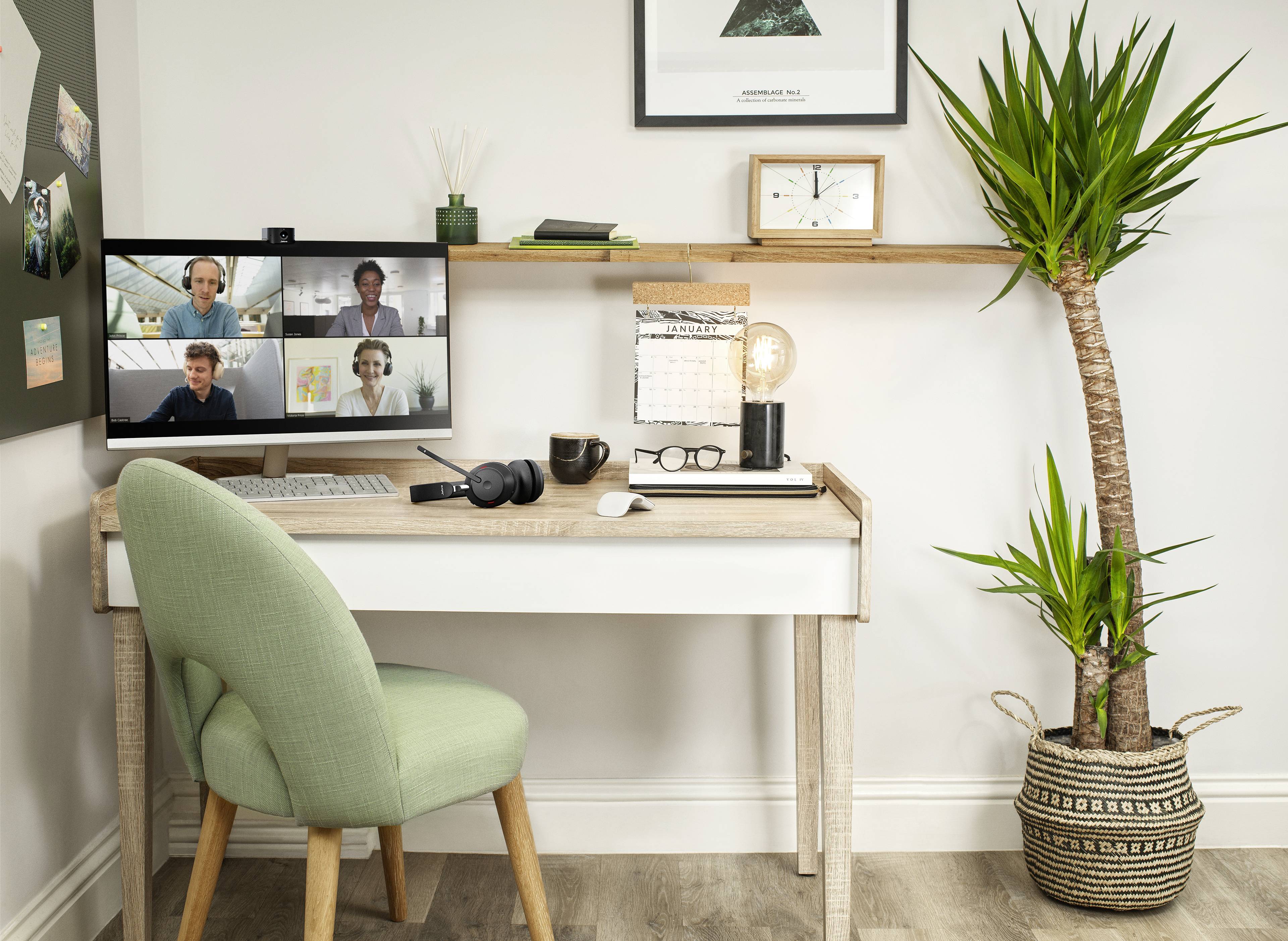 Et hjemmekontor med et skrivebord, hvorpå der er en computer med en videokonference i gang. Ved siden af er der en plante og en lampe.