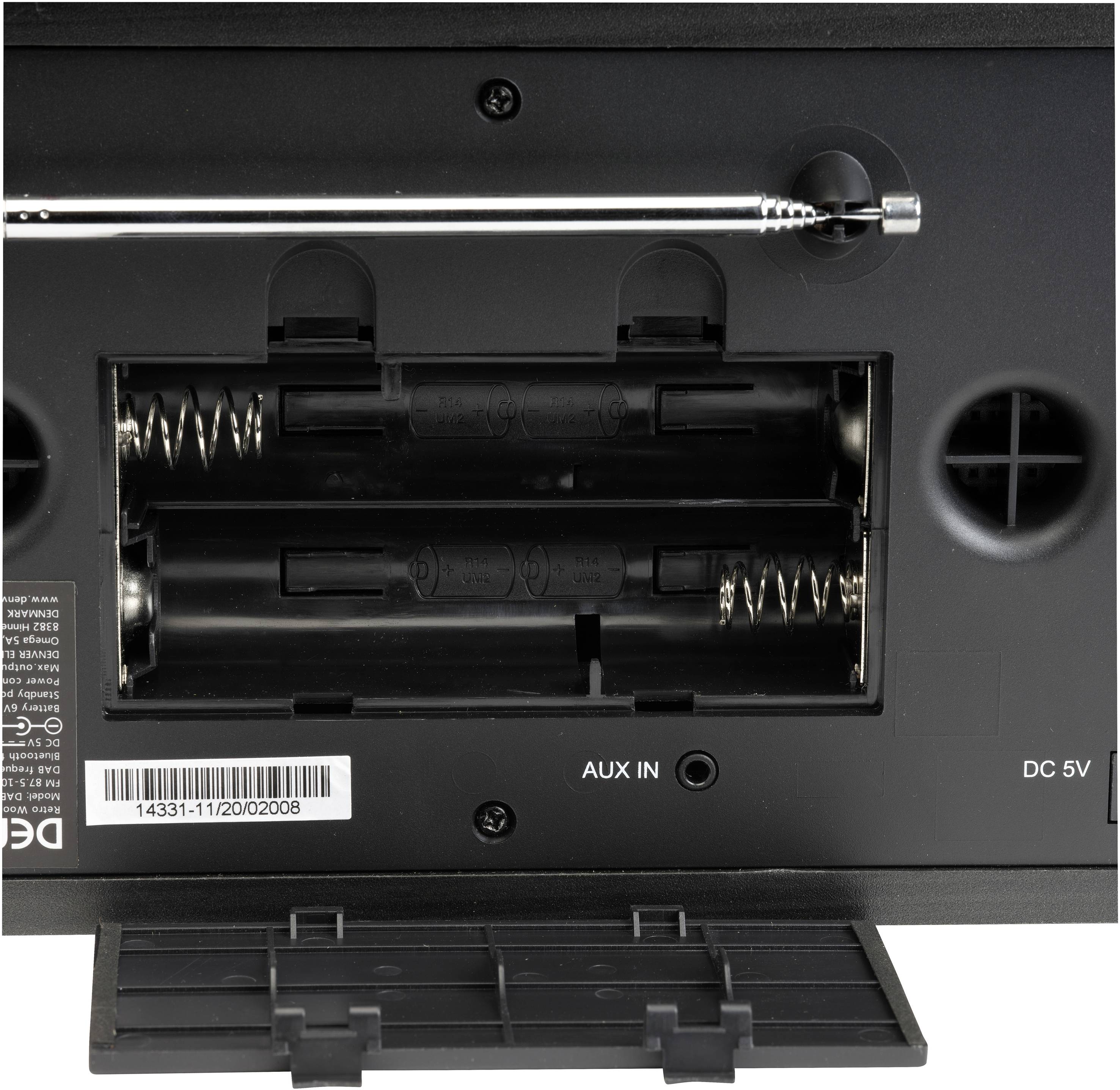 Batterirummet på en elektronisk enhed set nedefra, åbnet med synlige batterikontakter. Aux-indgang på højre side.