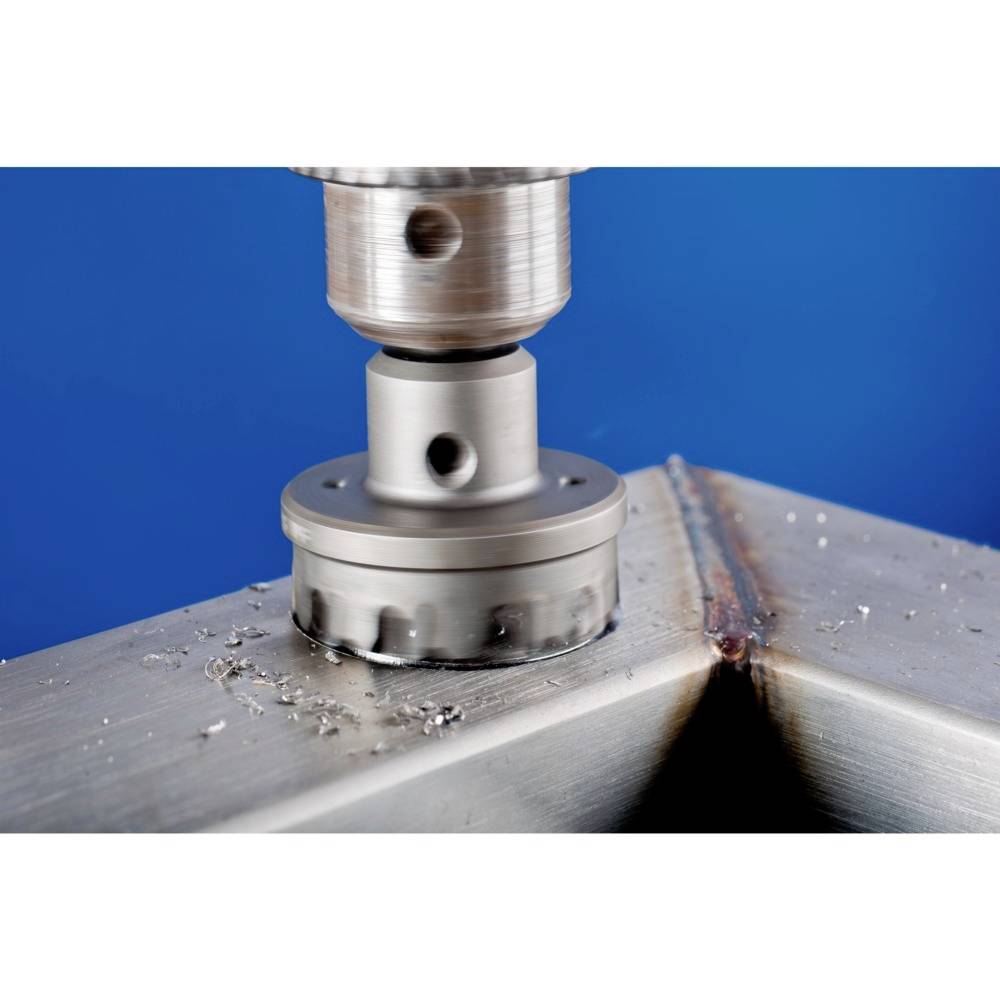 En bor bearbejder en metaloverflade ved en svejsning. Metalspåner er synlige. Baggrunden er blå.