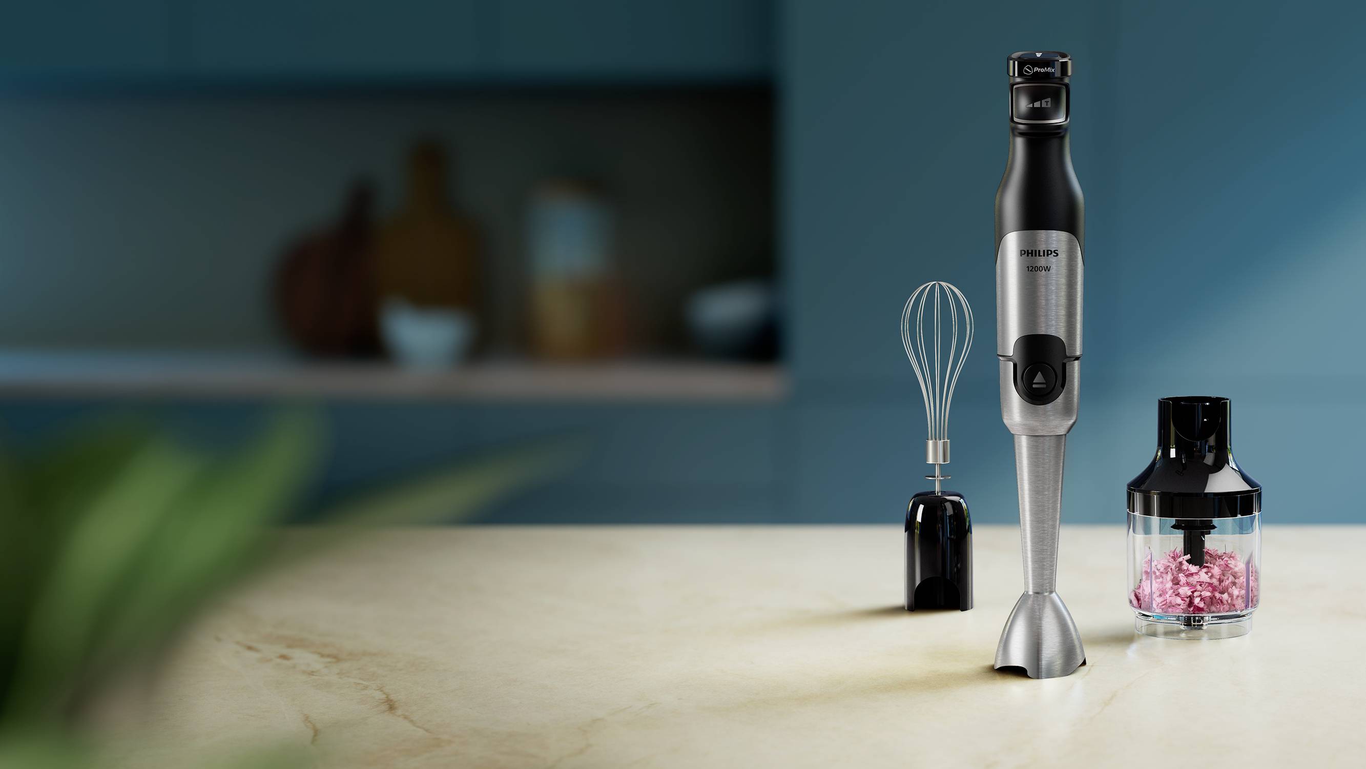 En stavblender med tilbehør, herunder en piskeris og en hakker, på et køkkenbord. I baggrunden uskarpe køkkenredskaber.