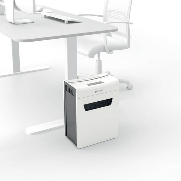 En hvid dokumentmakuleringsmaskine står på gulvet ved siden af et moderne skrivebord og en kontorstol.