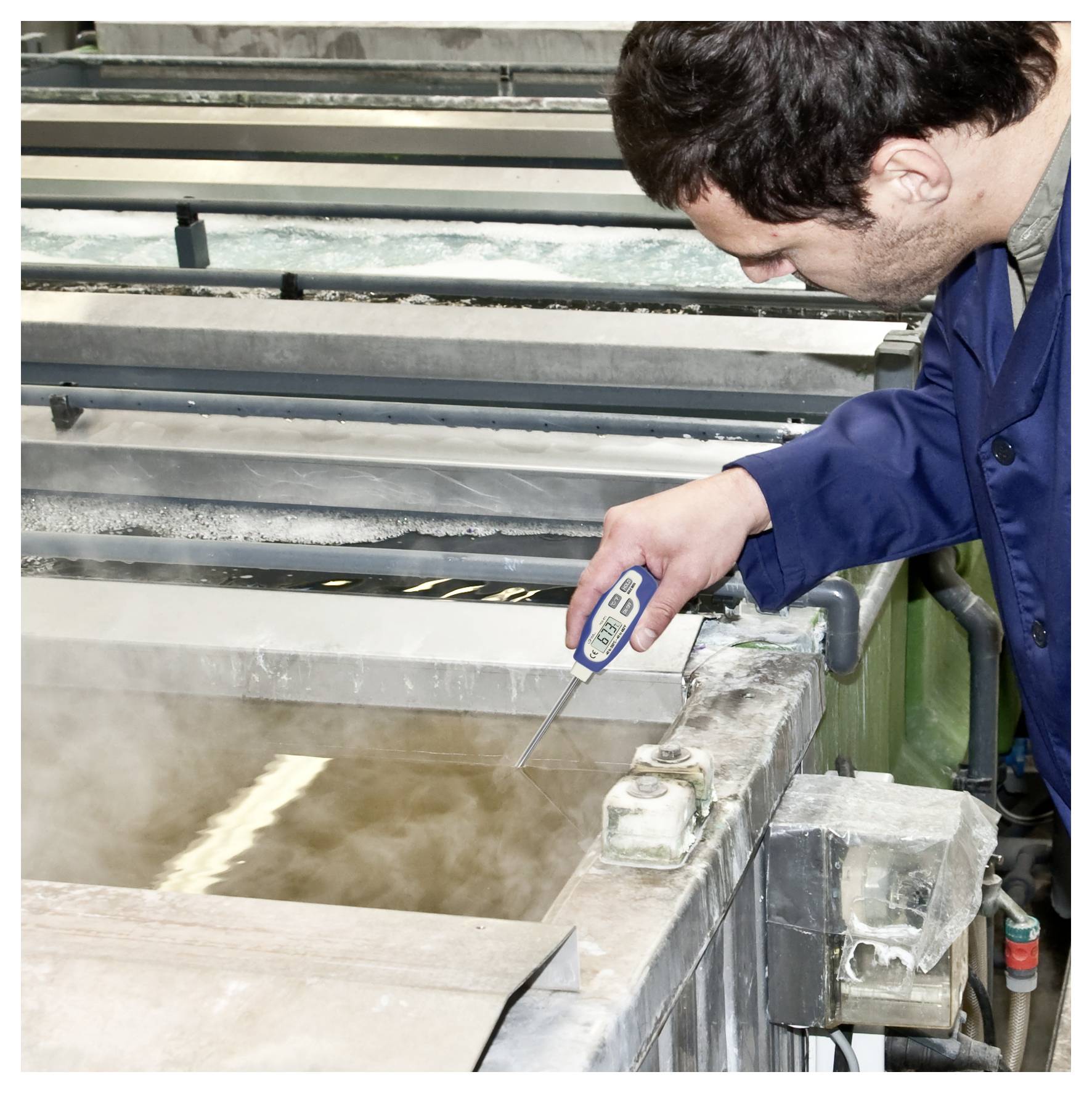 Arbejder måler temperatur i en dampende industriel tank med en digital måler.