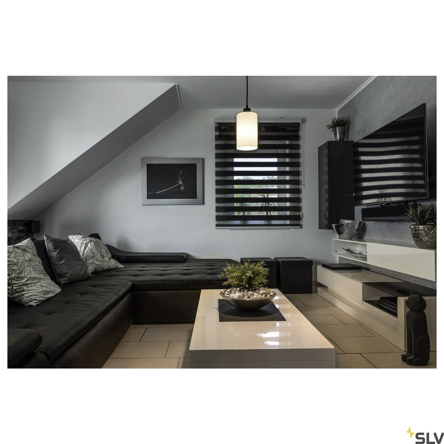 Hyggelig stue med mørk sofa, lyst sofabord, moderne lamper. Vindue med persienner, planter dekorativt placeret.