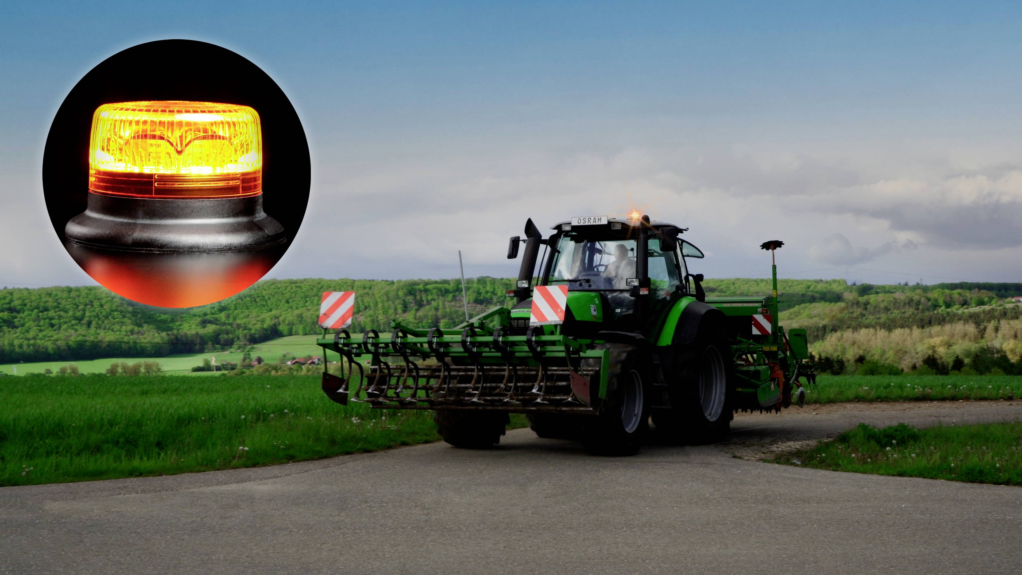 En traktor på en vej på en mark med en nærbillede af et gult advarselslys. Skove og himmel i baggrunden.