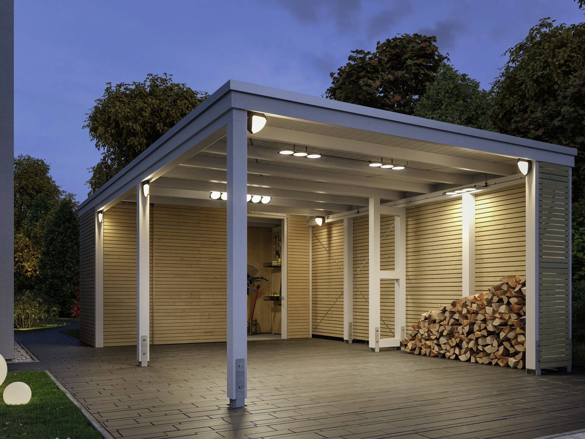 En moderne carport med sideværts træbeklædning, belyst om natten. Til venstre er en stak ved stablet under overdækningen.