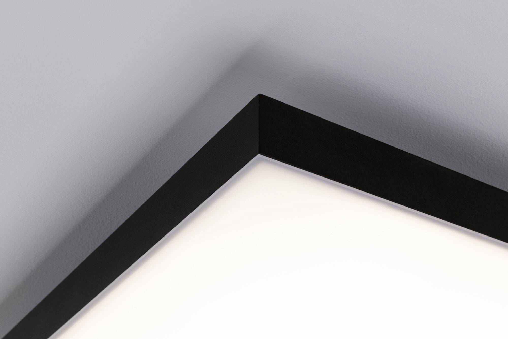 Hjørne af et rum med en moderne, sort loftslampe, der lyser varmt hvidt. Rene linjer og enkelt design.