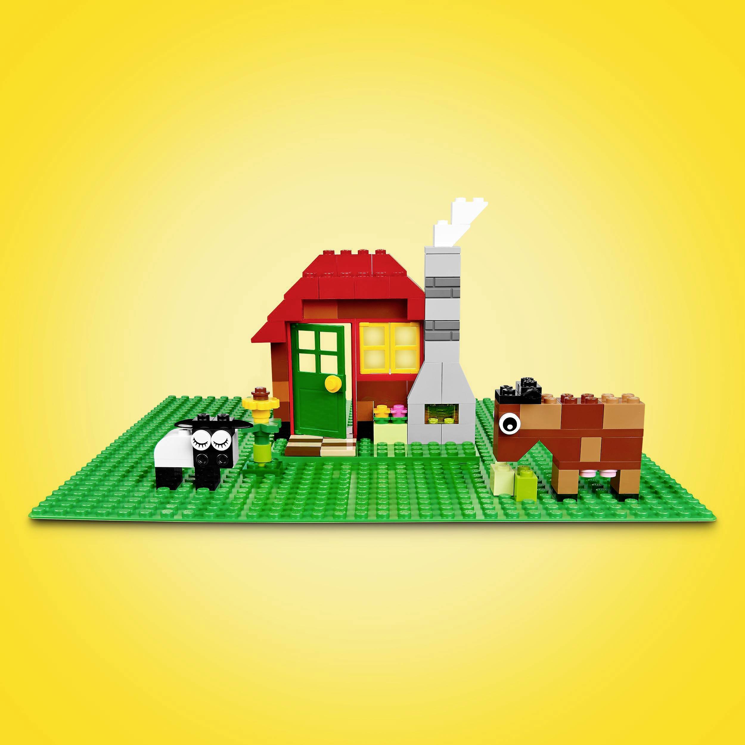 Lille Lego-scene med et rødt hus, skorsten, grøn dør, et får og en ko på en grøn basisplatte foran en gul baggrund.