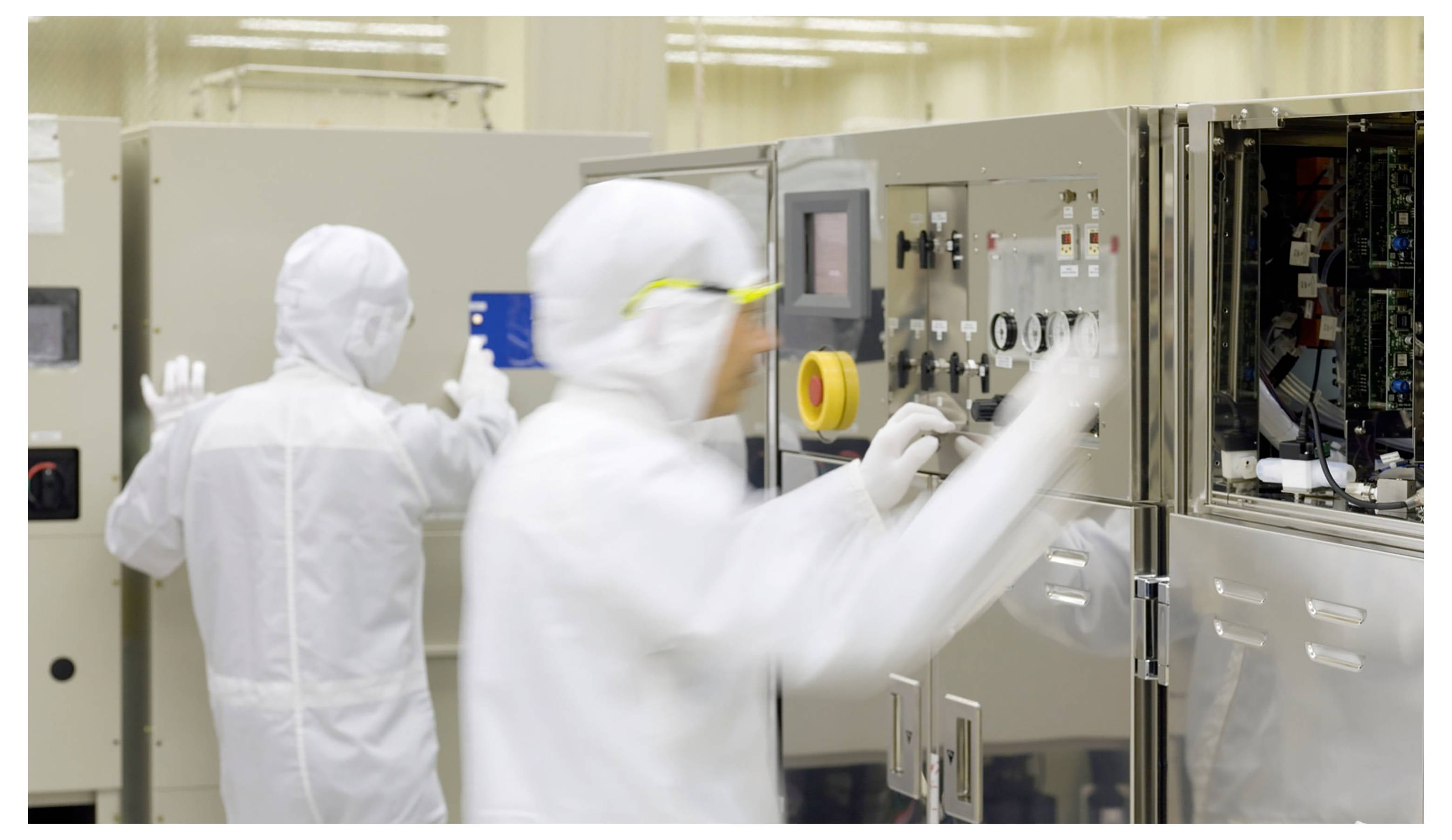 To technicians i renrumsdragter betjener industrielt maskineri i et laboratorium eller produktionsanlæg.