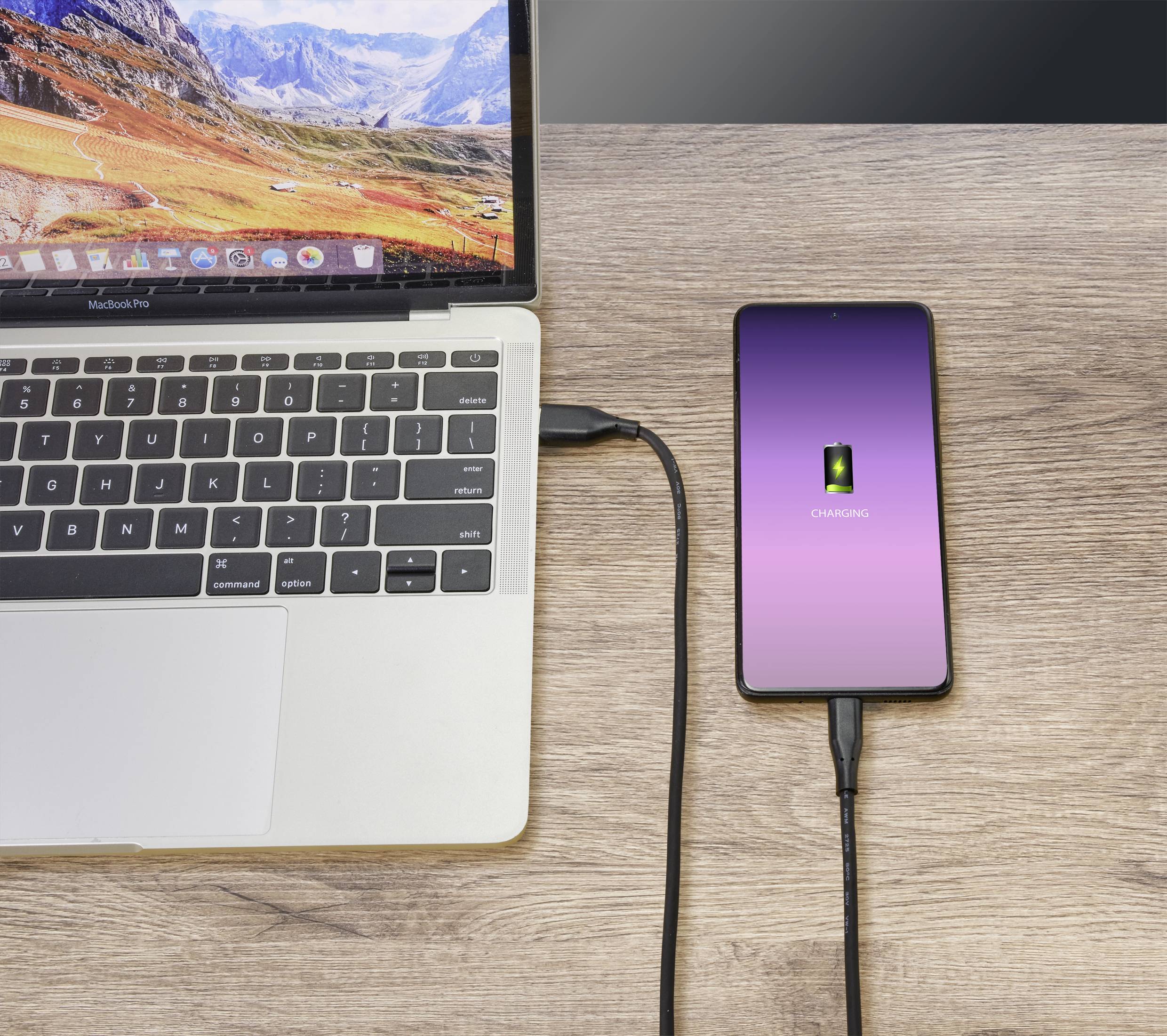 En bærbar computer forbinder sig via et kabel til en smartphone, der oplades. Telefonens skærm viser en grøn batterimåler.