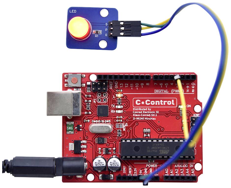 Et rødt mikrocontroller-printplade forbundet med kabler til en blå sensor, som indeholder en rød LED og en gul knap.