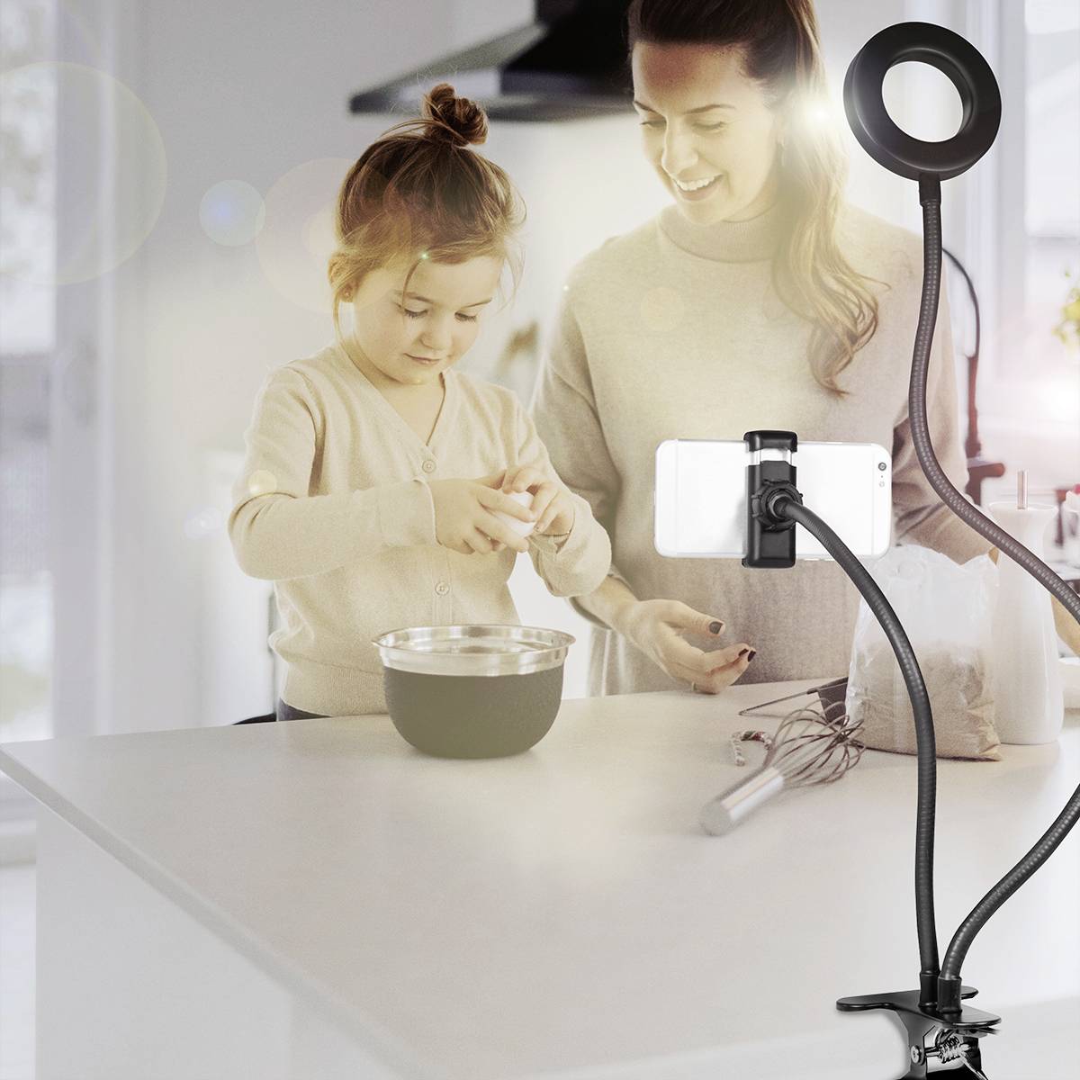 En kvinde og et barn forbereder ingredienser i et køkken. En mobiltelefon med ringlys er rettet mod arbejdsfladen.