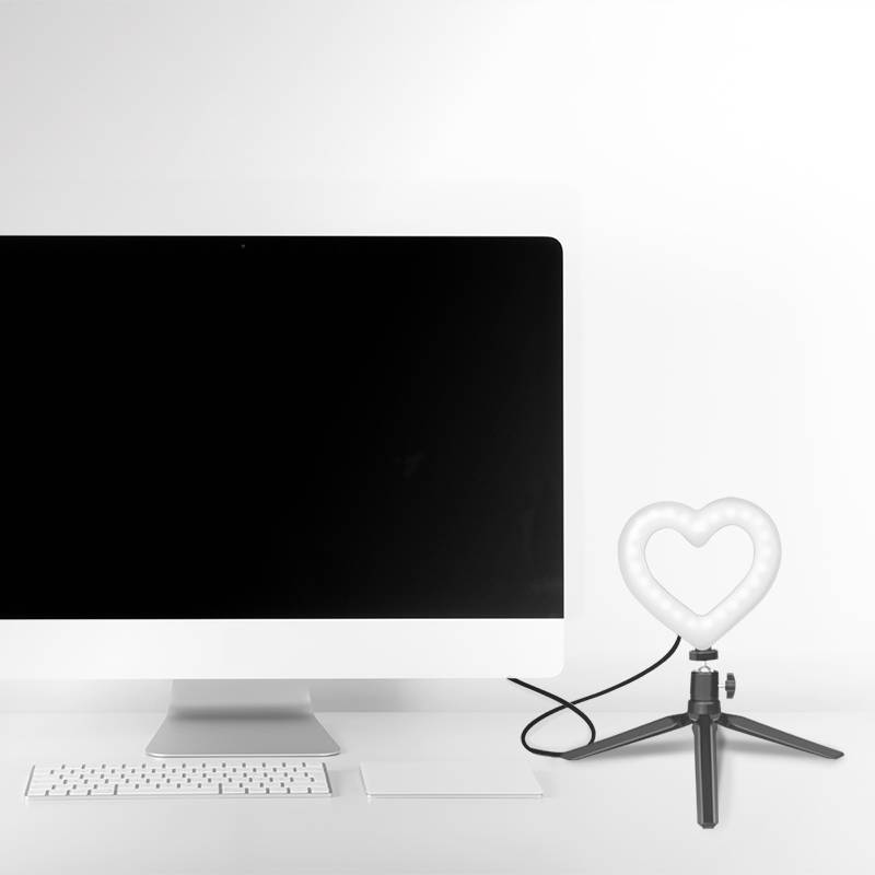 En computerskærm med sort display står på et skrivebord. Ved siden af den er der en holder med en hjertedannet lampe.