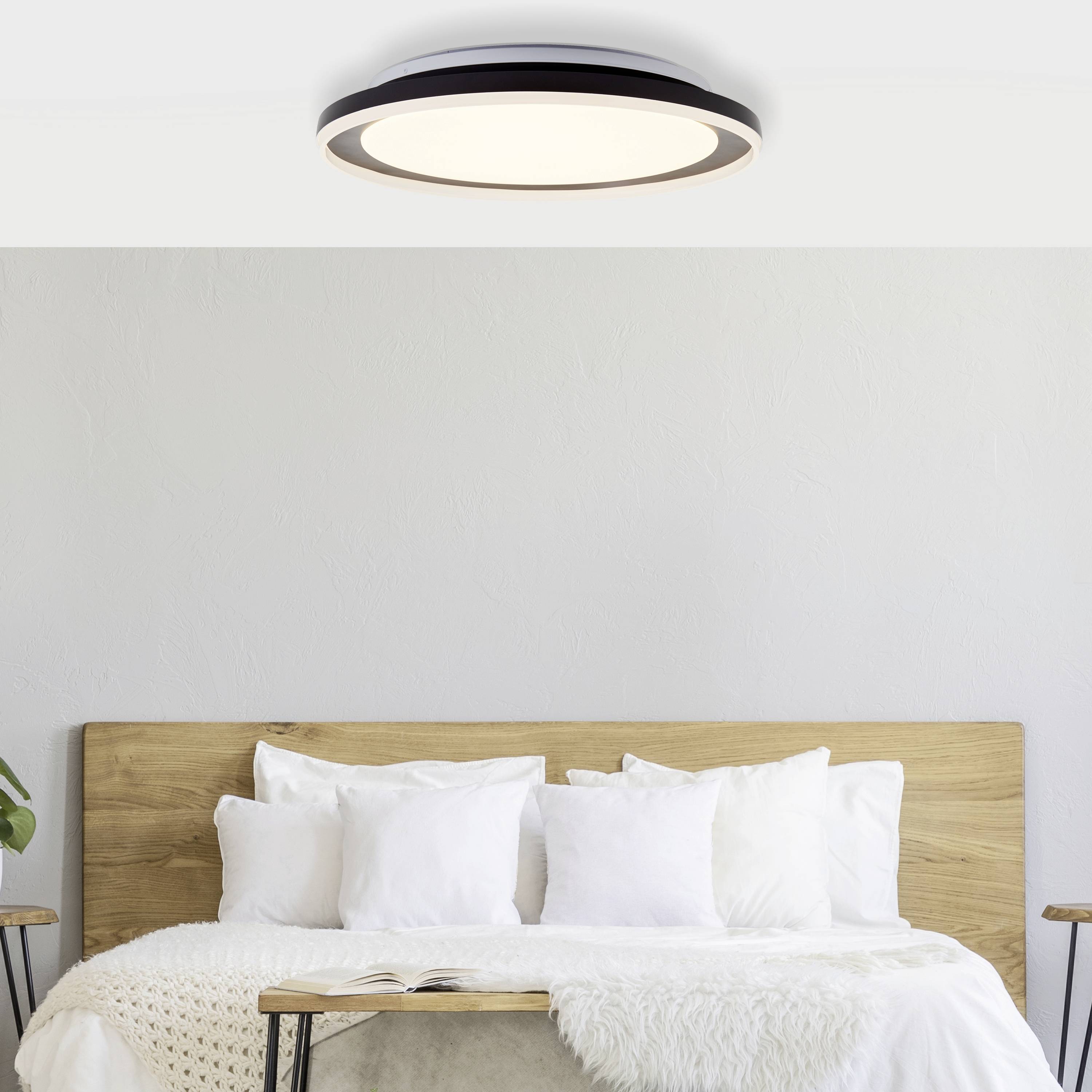 Et moderne soveværelse med en træseng, hvide puder, et tæppe og en rund loftslampe over sengen.