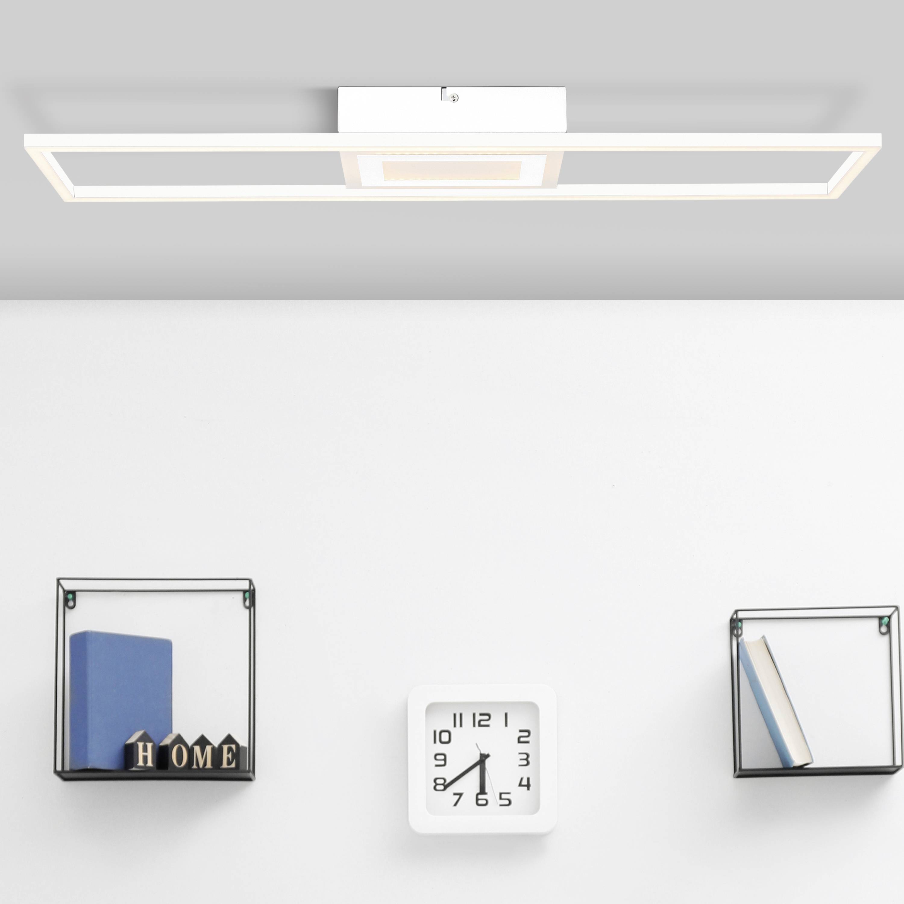 Minimalistisk vægdesign med et rektangulært, hvidt LED-lys i loftet. Herunder to væghylder med dekoration og et ur.