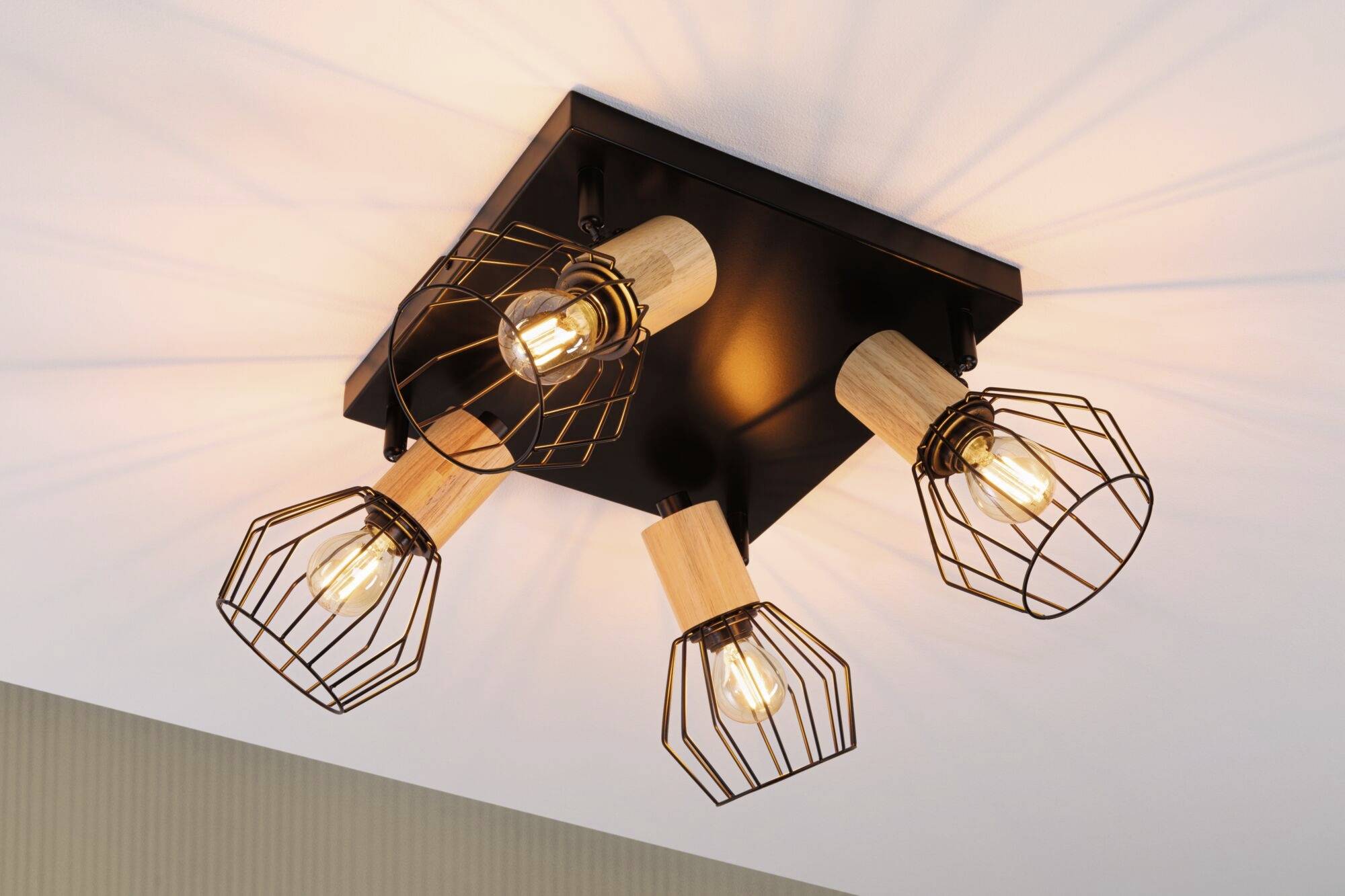 Loftslampe med fire glødepærer i trådnet, monteret på træcylindre på et sort firkantet grundlag.