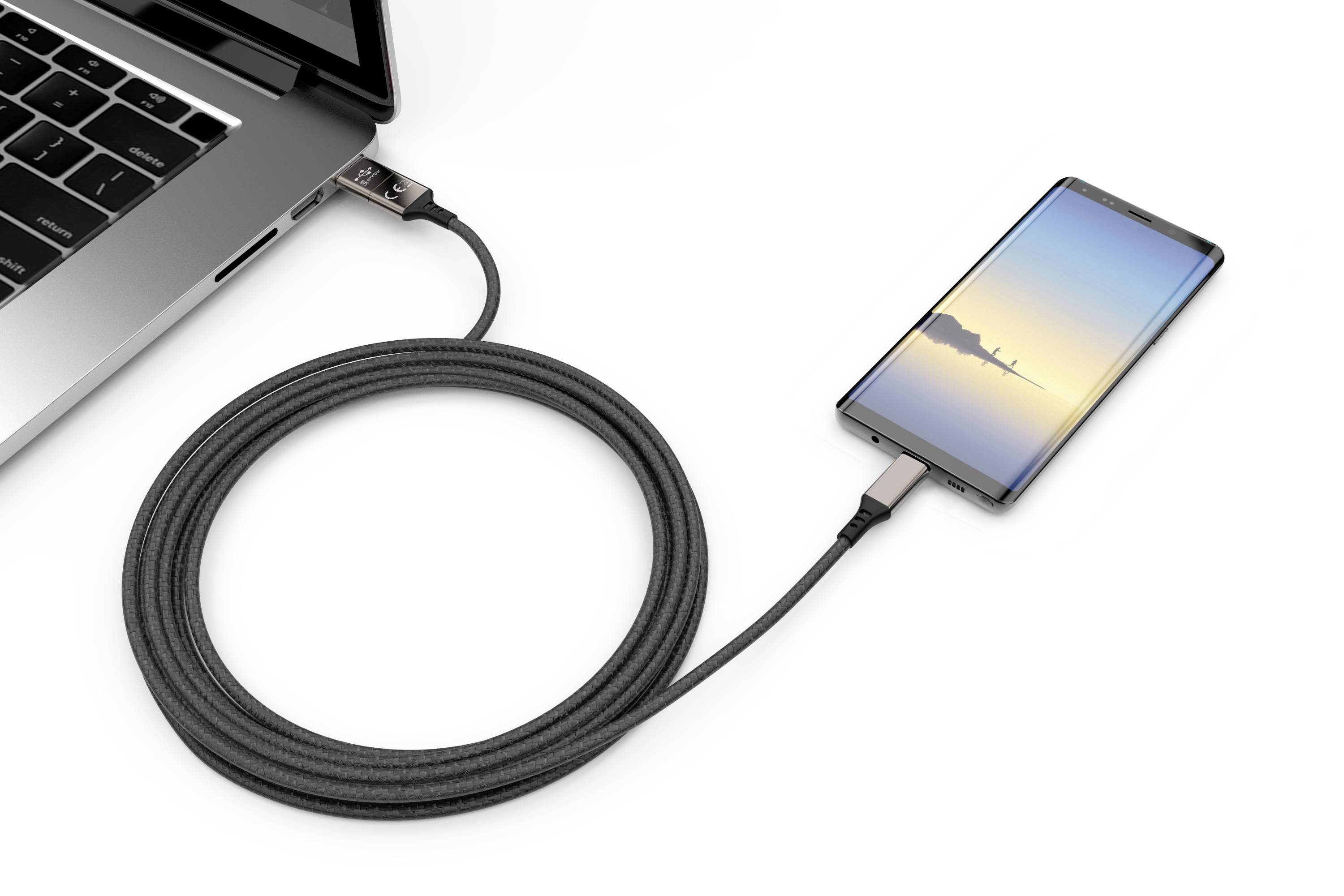 En smartphone oplades via et kabel tilsluttet en bærbar computer. Smartphonen viser en solnedgangsbaggrund.