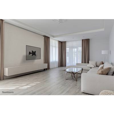 Minimalistisk stue med cremehvid sofa, glaskaffe bord, vægmonteret tv-beslag og store vinduer med gardiner.
