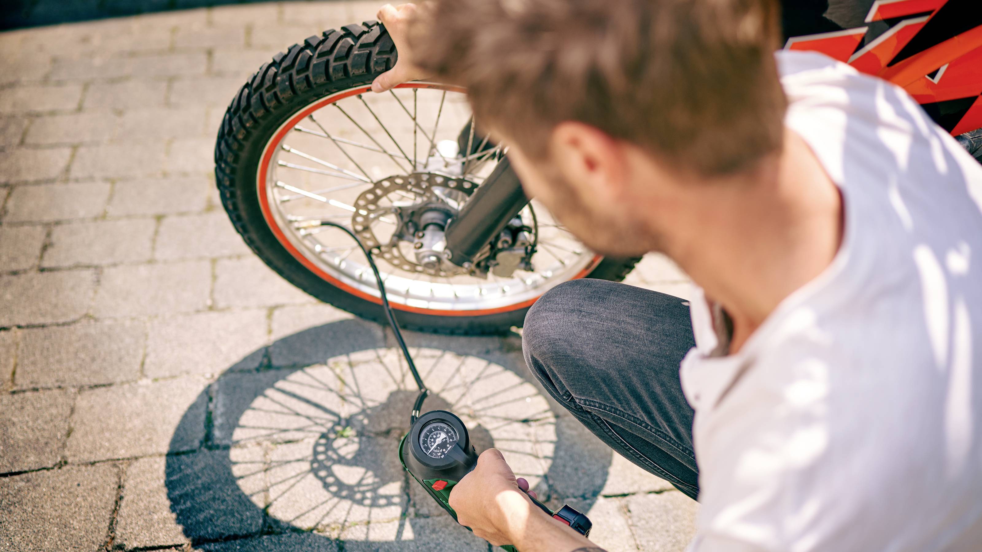 En mand pumper et cykeldæk. Han tjekker lufttrykket med et manometer. Cyklen står på en brolagt sti.