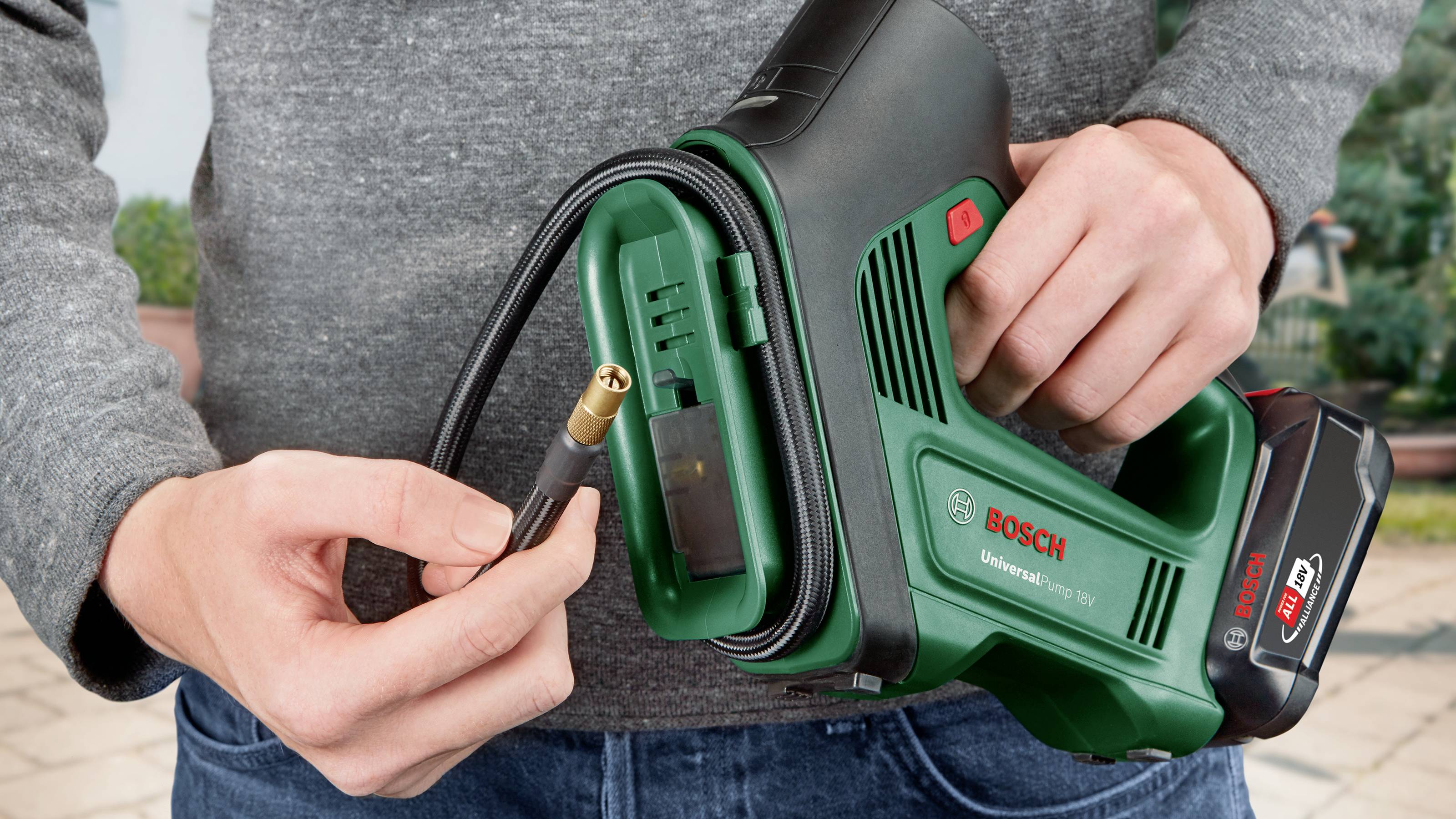 En person holder en grøn Bosch-håndkompressor, klar til at fastgøre slangen til et tilslutningspunkt.