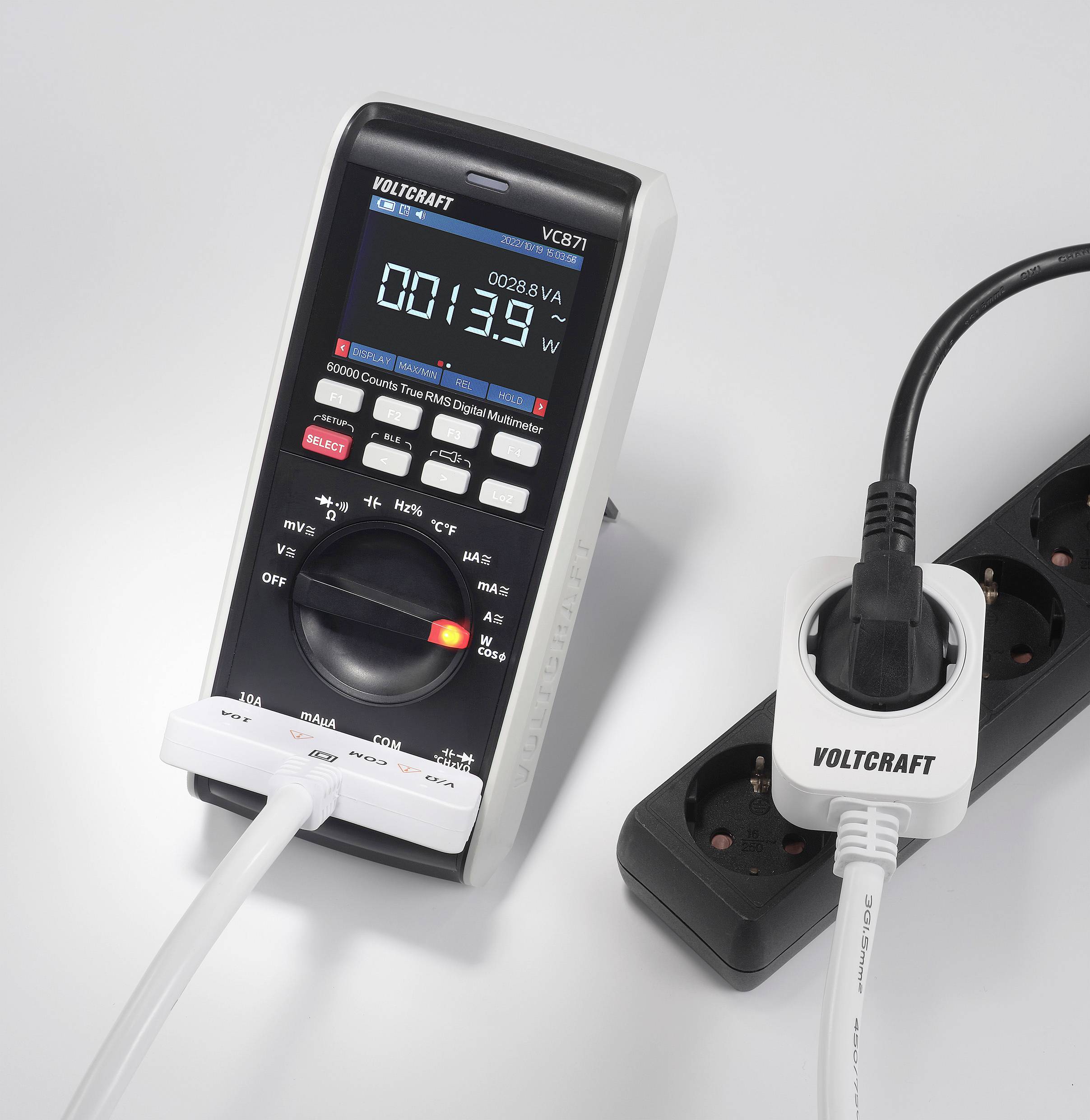 Et digitalt multimeter måler strømstyrke, forbundet med en forlængerledning, som er sat i et stikdåsepanel.