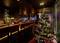 Et festligt pyntet juletræ med farverige lys står i en stemningsfuldt belyst restaurant eller bar.