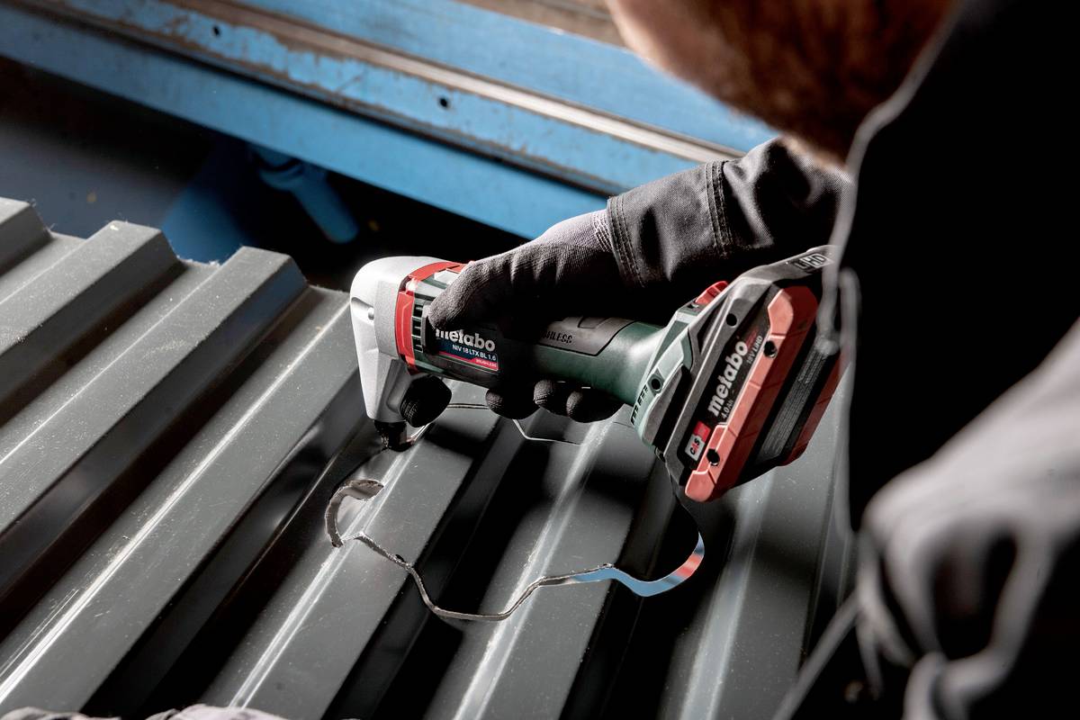 En person skærer en bølgeplade med et Metabo elektrisk værktøj, omgivet af et metallisk miljø.