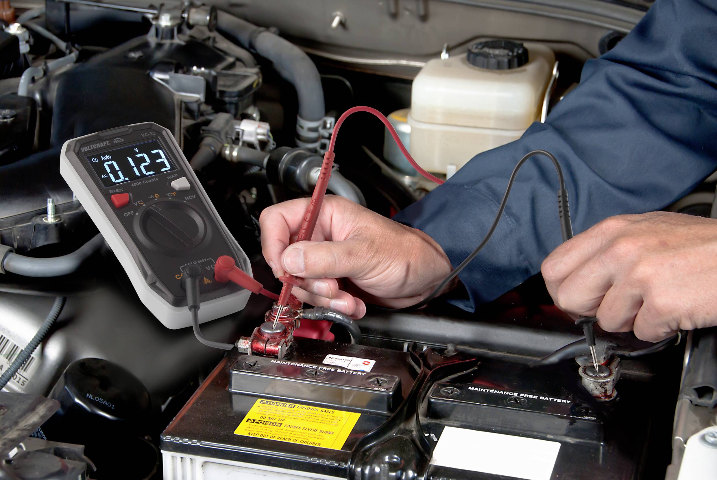En mekaniker måler spændingen på en bilbatteri med et multimeter. Displayet viser 0,123 volt.