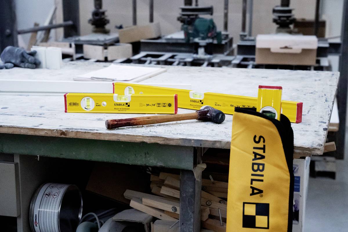 Et værksted med flere røde og gule vaterpas på et bord, ved siden af en hammer og en gul Stabila-taske.