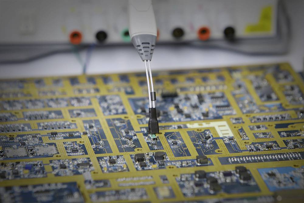 Et testapparat undersøger kredsløb på et printplade. Elektriske forbindelser og komponenter er synlige.