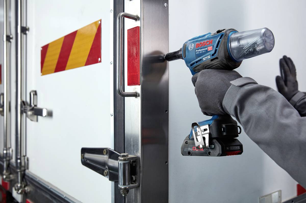 En person fastgør døren på en varevogn med en blå akku-skruetrækker. Døren har røde og gule reflektorer.