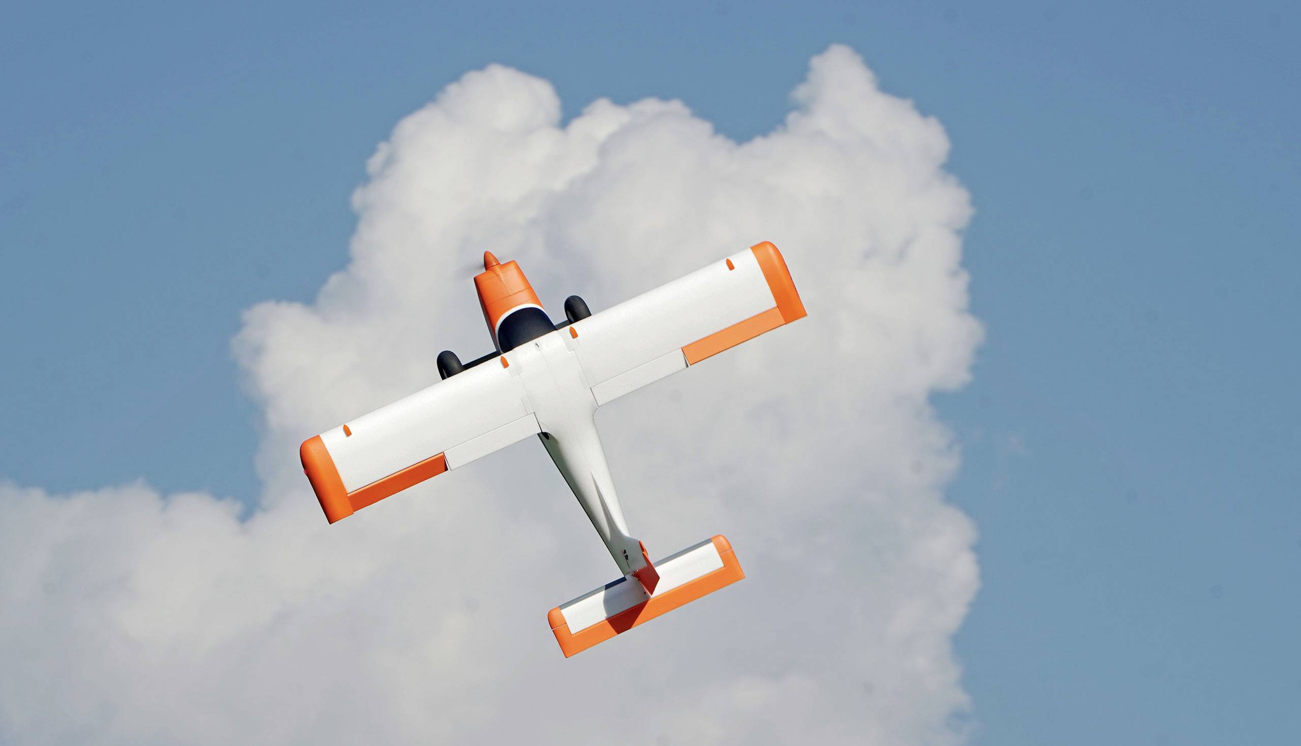 Et lille, orange-hvidt fly flyver mod en baggrund af blå himmel og hvide skyer.