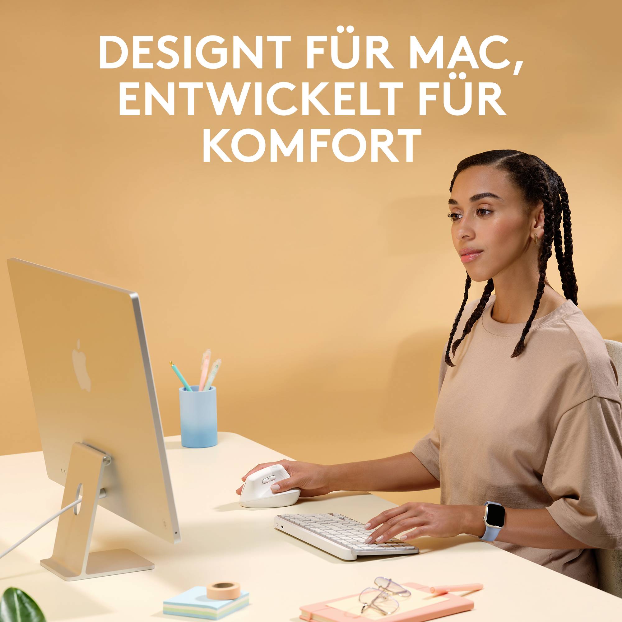 En kvinde sidder ved et skrivebord, bruger mus og tastatur, med teksten 'DESIGNET TIL MAC, UDVIKLET TIL KOMFORT' i baggrunden.