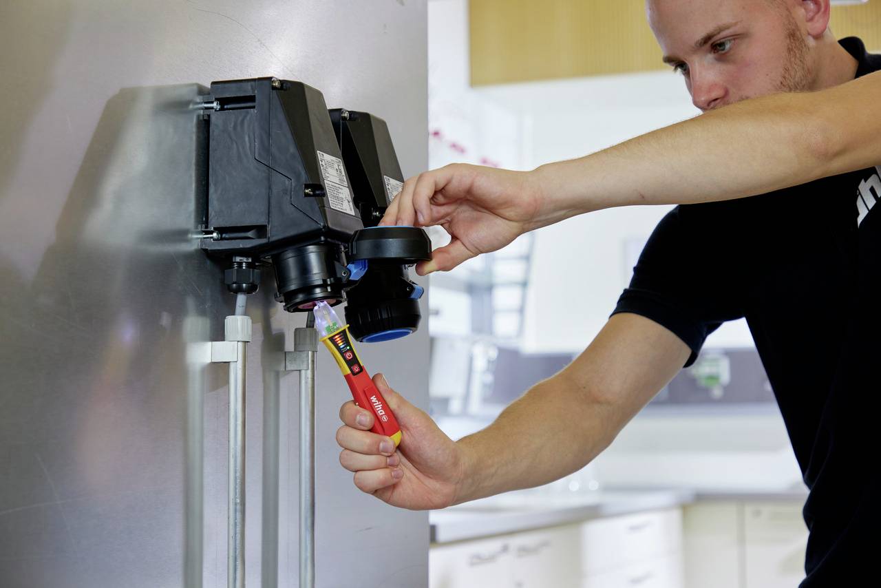 En mand kontrollerer en elektrisk enhed med en spændingstester for at sikre sikkerheden og funktionaliteten.