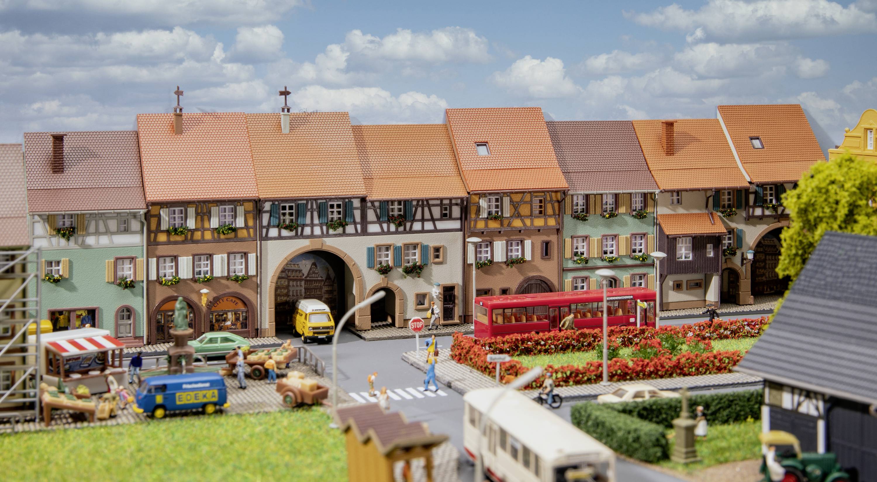 En miniaturemodel af en by med bindingsværkshuse, en rød bus og biler på gaden. Scenen viser et travlt, landligt miljø.