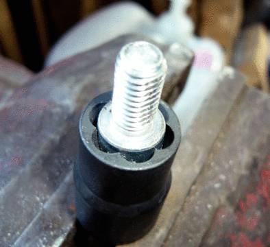 Metalskrue med delvist gevind i sort plastikbeklædning. Skruen er i fokus, baggrunden er sløret.