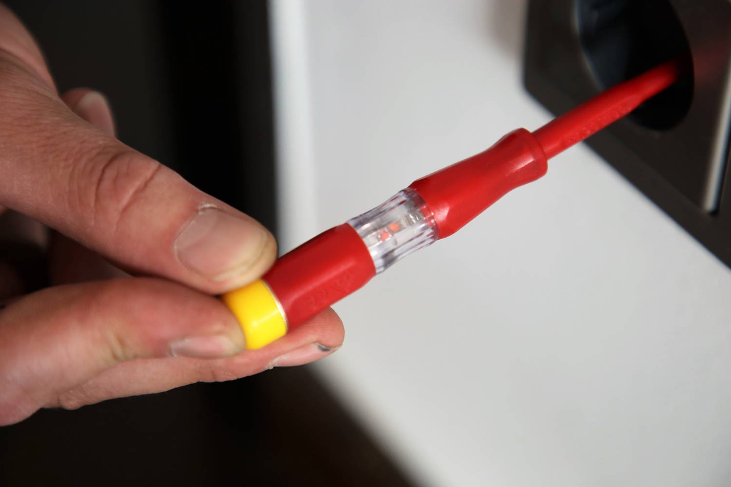 En hånd stikker en spændingstester med rødt håndtag i en stikkontakt for at kontrollere den elektriske spænding.