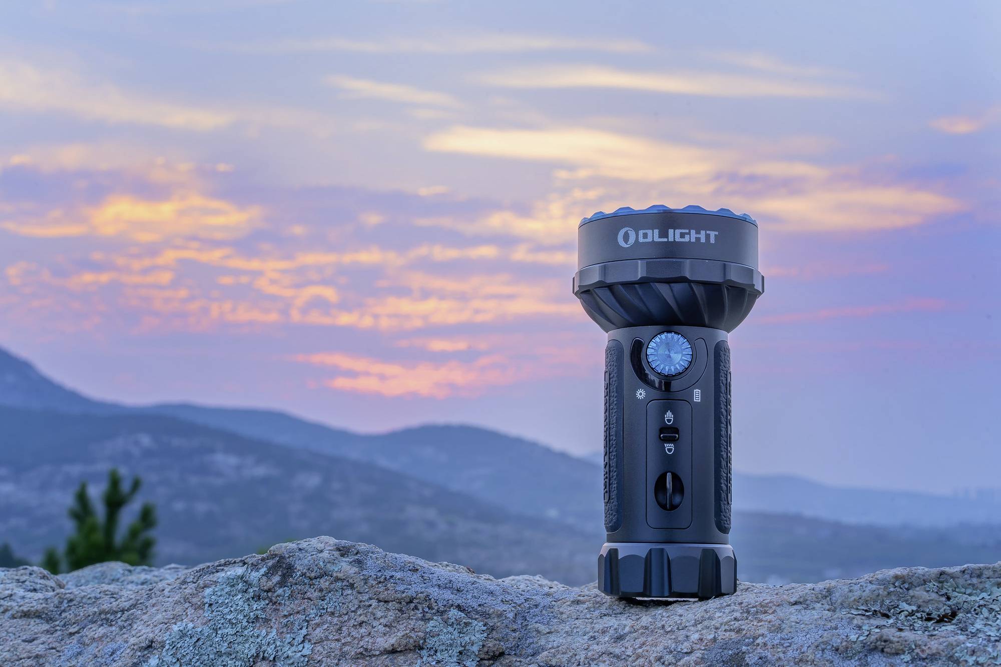 En lommelygte hviler på en klippe, med en farverig solnedgang over et bakket landskab i baggrunden.