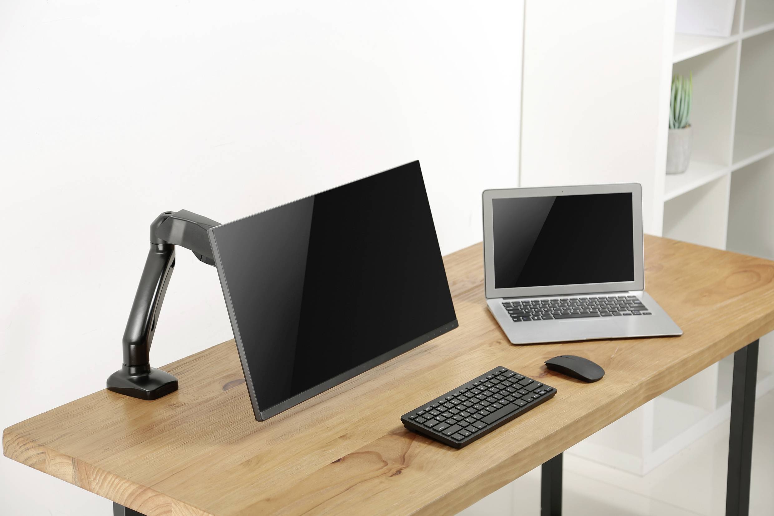 Et skrivebord med en bærbar computer, en stor, armhængt skærm, et tastatur og en mus.