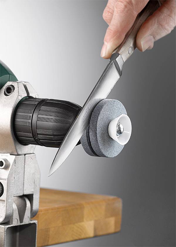 En hånd sliber en kniv ved et roterende slibemaskine. Slibestenen drejer hurtigt, og kniven holdes i den korrekte vinkel.